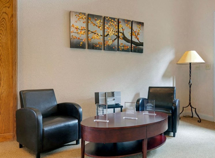 Resident lounge center with canvas painting on wall, wooden coffee table, and two leather accent chairs